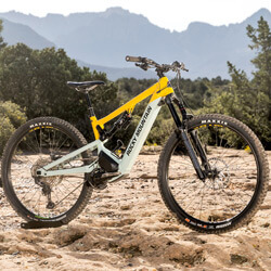 Thumbnail photo of yellow and sky-blue full-suspension E-MTB on a field of slickrock with a mountain silhouette in the background.